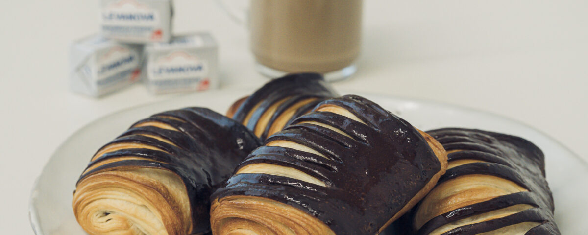 Tres napolitanas de chocolate a dos colores en un plato junto a cubos de levadura fresca Levanova y un vaso de café