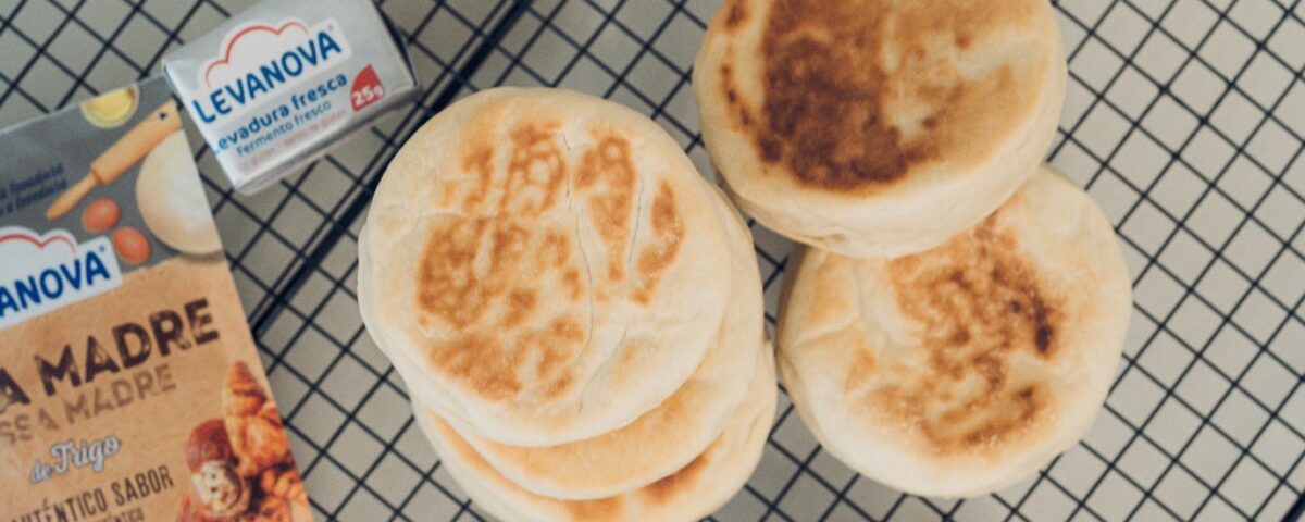 Varios English Muffins redondos y tostados apilados sobre una rejilla negra, acompañados de levadura fresca y masa madre Levanova
