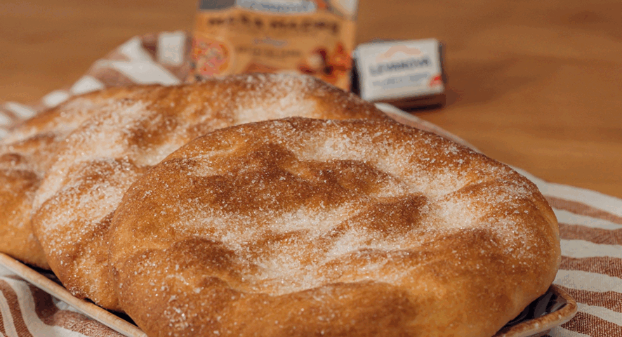 Una generosa torta de manteca manchega, dorada y con una textura rústica y burbujeante, sobre una mesa de madera con un paño de cocina de cuadros