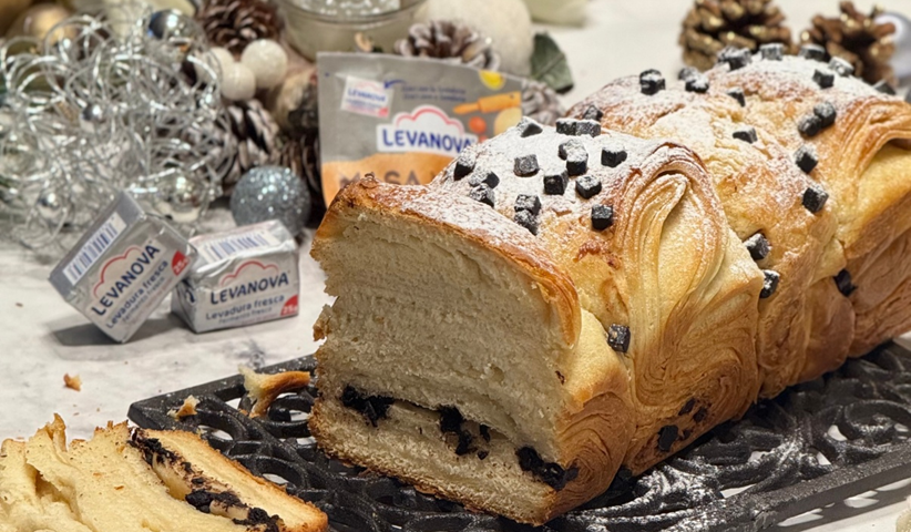 Primer plano de un pan de croissant cortado con capas de hojaldre y chocolate, decorado con azúcar glass y rodeado de adornos navideños
