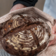 Manos sujetando una hogaza de chocolate y naranja envuelta en un paño de cocina de rayas