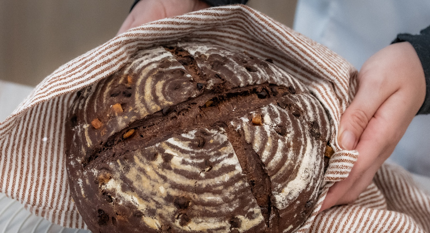 Manos sujetando una hogaza de chocolate y naranja envuelta en un paño de cocina de rayas