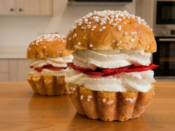 Dos bollos de brioche con azúcar perlado, rellenos de nata montada y fresas laminadas, sobre una mesa de madera