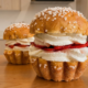 Dos bollos de brioche con azúcar perlado, rellenos de nata montada y fresas laminadas, sobre una mesa de madera