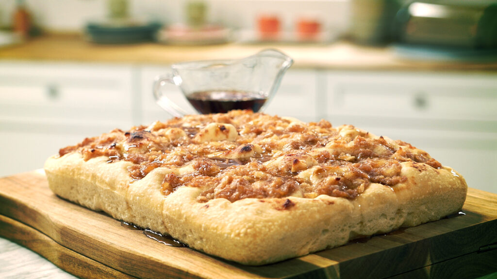Focaccia de manzana caramelizada con canela sobre tabla de madera y jarra de sirope