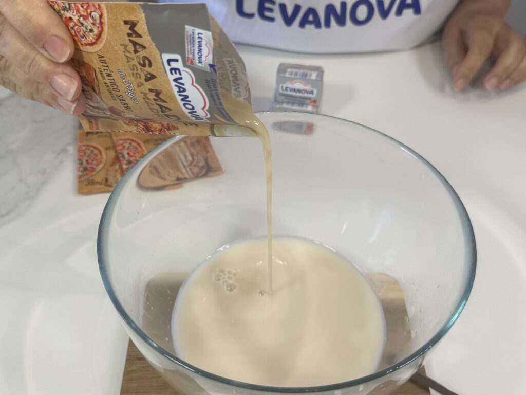 Persona vertiendo el contenido de un sobre de masa madre Levanova en un bol con agua tibia para preparar bollicaos caseros