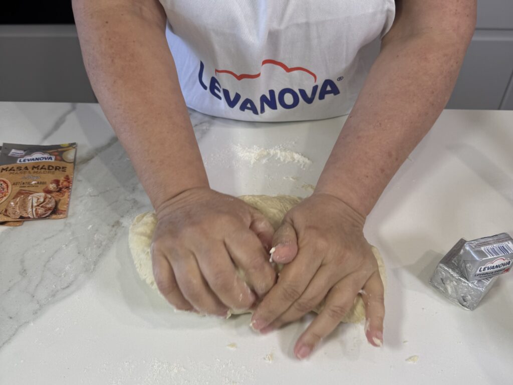 Primer plano de unas manos amasando una masa elástica y suave sobre una encimera blanca para preparar bollicaos