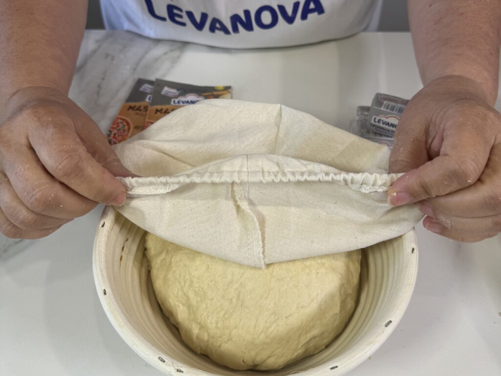 Masa de bollicaos caseros fermentando en un bol cubierto con un paño de lino