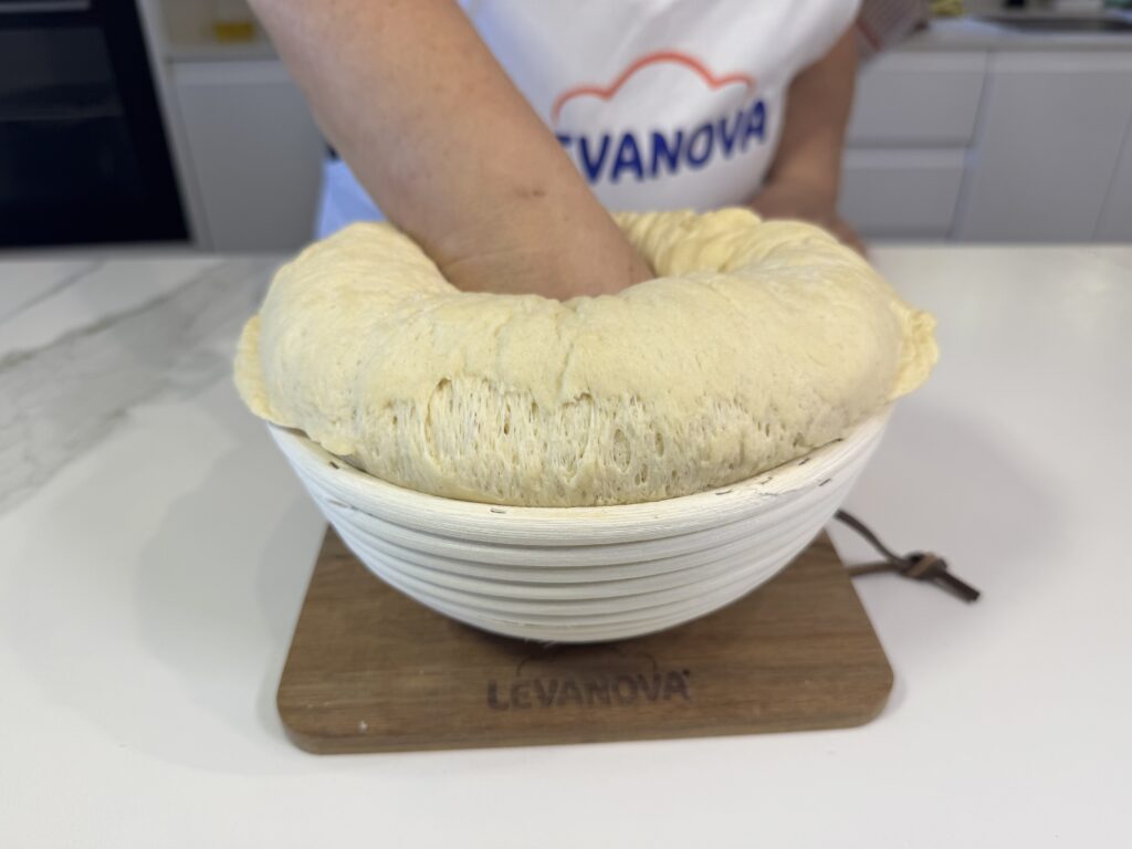 Mano presionando una masa fermentada en un bol blanco de Levanova para desgasificarla