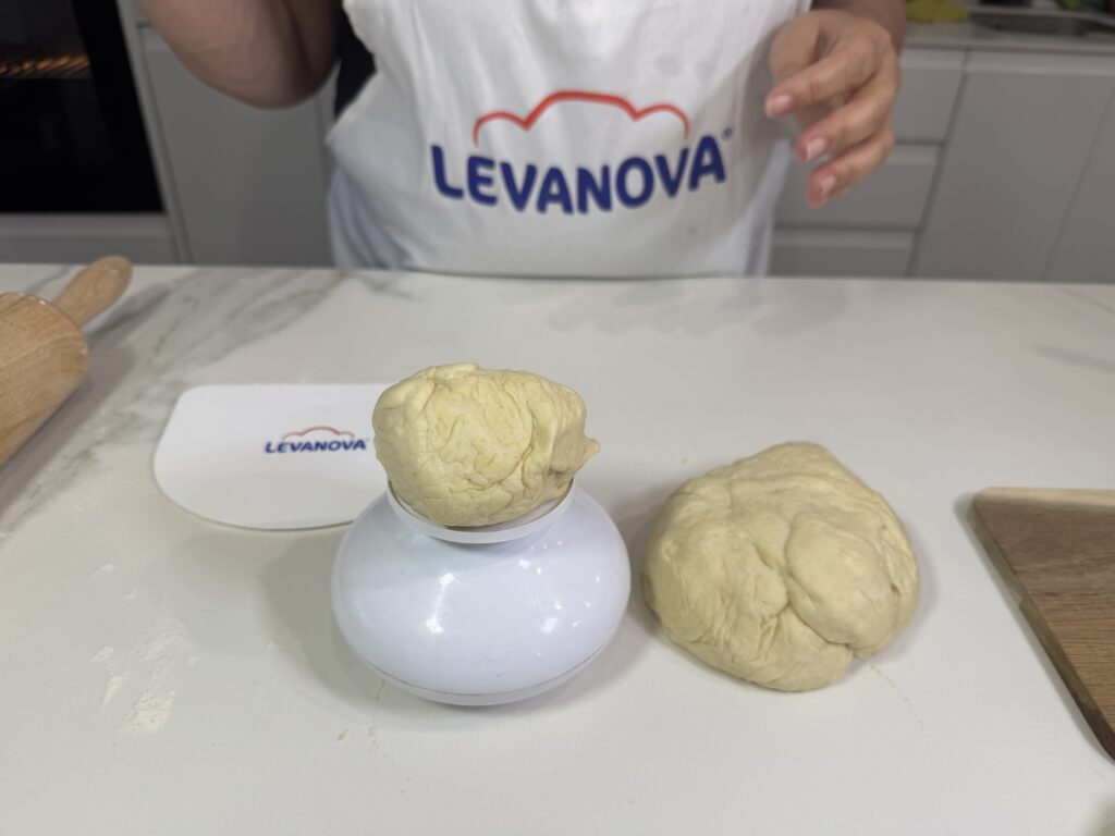 Una bola de masa sobre una báscula blanca de cocina junto a otra porción de masa en una encimera