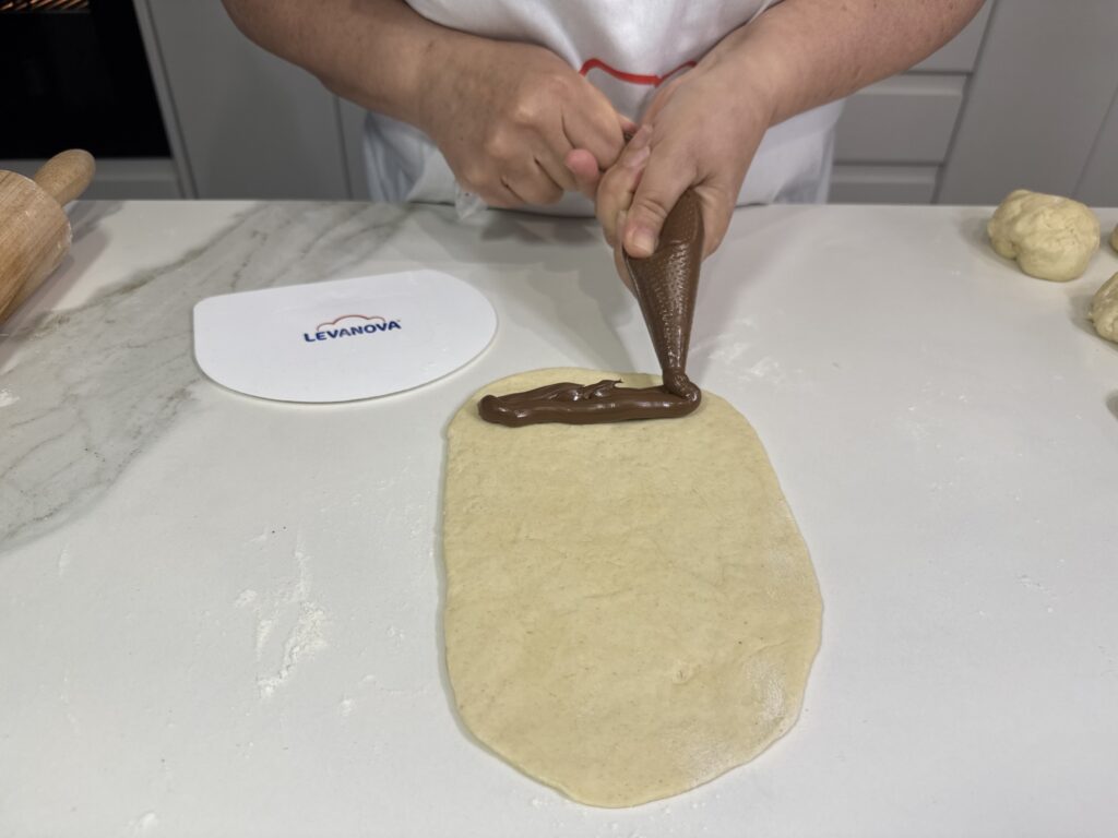 Persona utilizando una manga pastelera para aplicar una línea de crema de chocolate sobre una masa estirada en la encimera