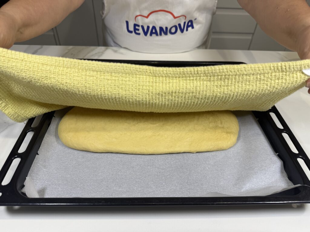 Masa estirada en la bandeja de horno tapada con un paño