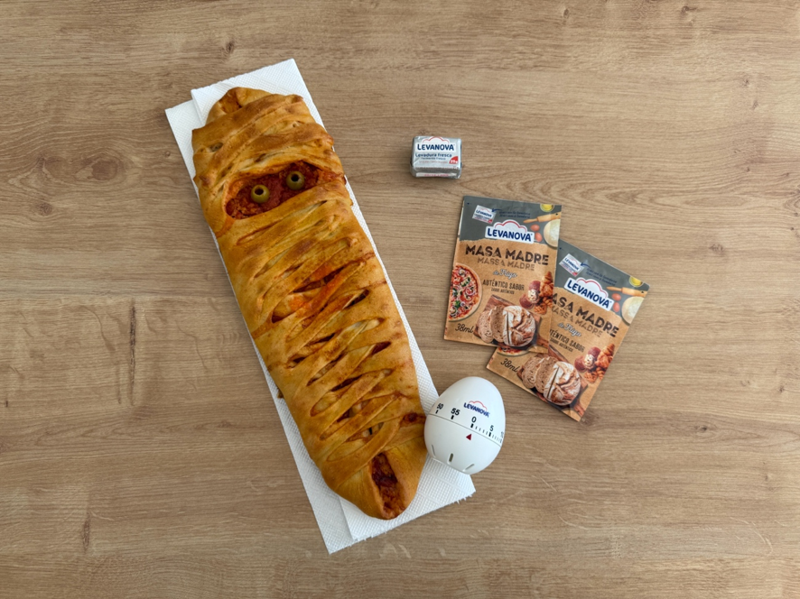 Pizza de Halloween con forma de momia, decorada con aceitunas como ojos y acompañada de productos de masa madre Levanova